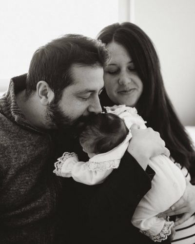 Fotografisanje beba kod kuće – mama i tata drže svoju bebu pored prozora uz prirodno svjetlo